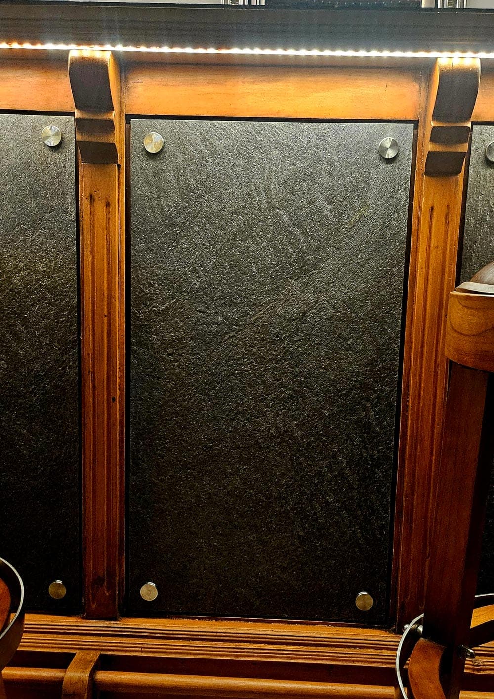 Möbelfüllung aus dunklem Stein im Holzrahmen, von Zierschrauben gehalten