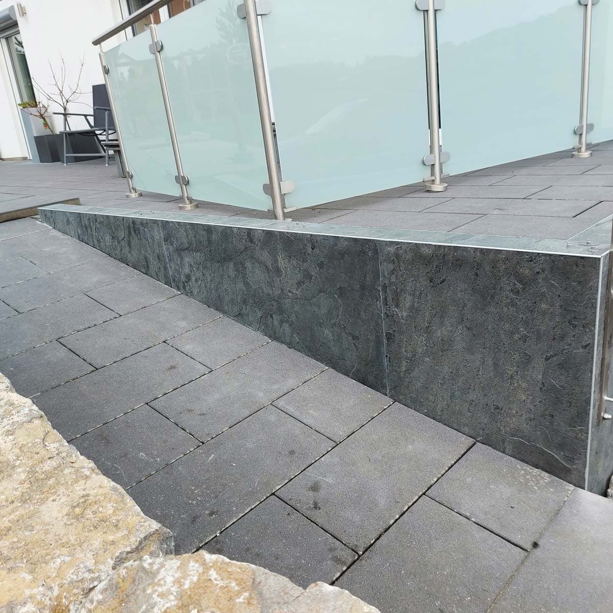 Terrassenmauer mit dunkler Steinverkleidung unter dem Glasgeländer