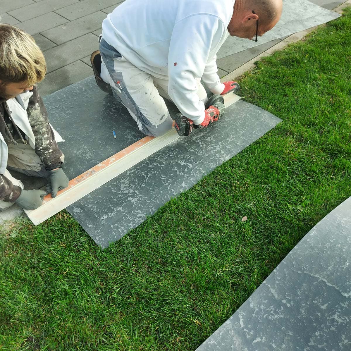 Eine großformatige Platte wird im Garten zugeschnitten: tragen und anlegen geht zu zweit, ohne Hebehilfe.